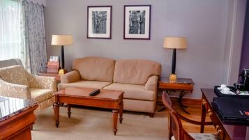 A living room with a beige sofa, two armchairs, a coffee table, a side table with a lamp, and framed artwork on the wall.