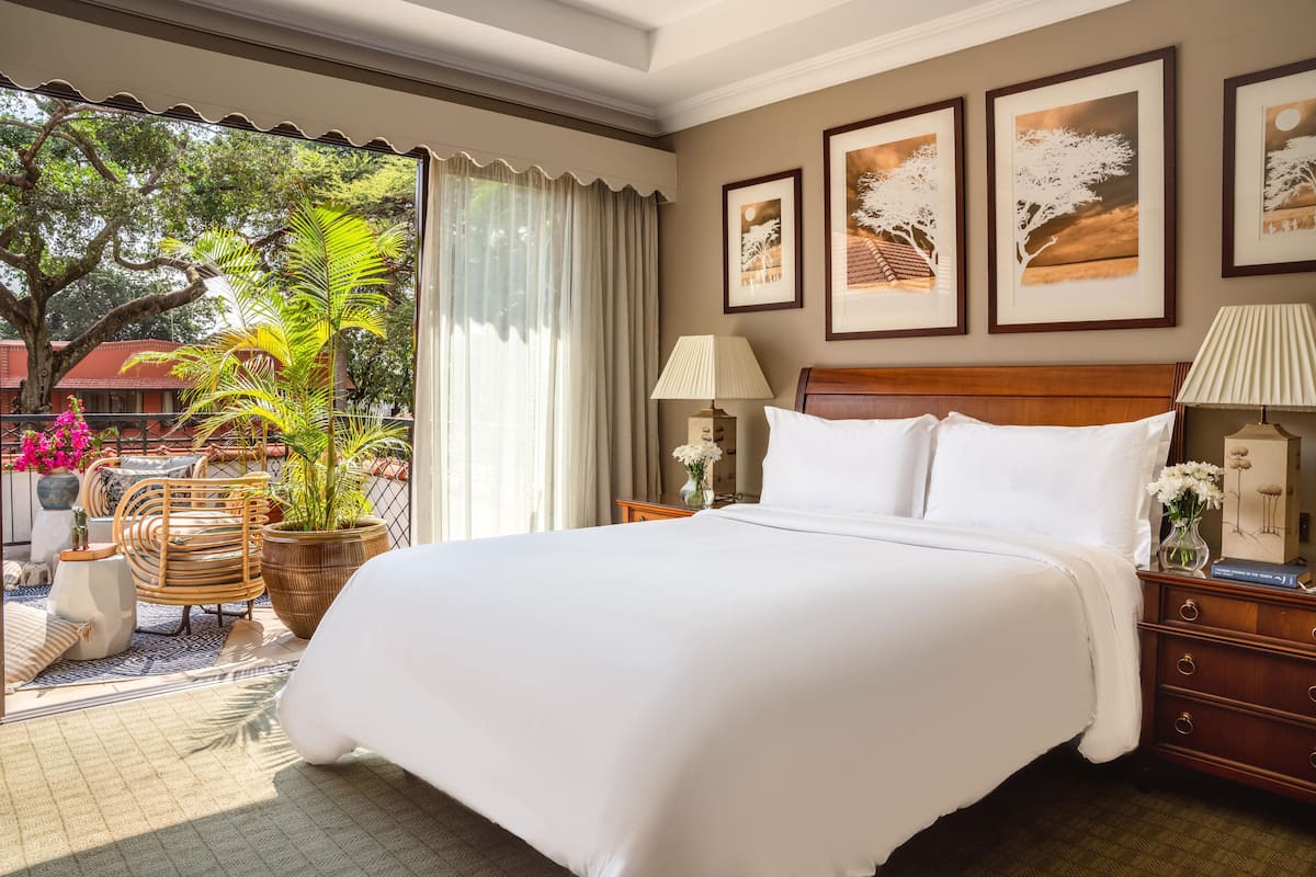 Quarto de hotel com uma cama grande, duas mesas de cabeceira, uma mesinha de apoio, uma janela com cortinas e obras de arte emolduradas na parede.