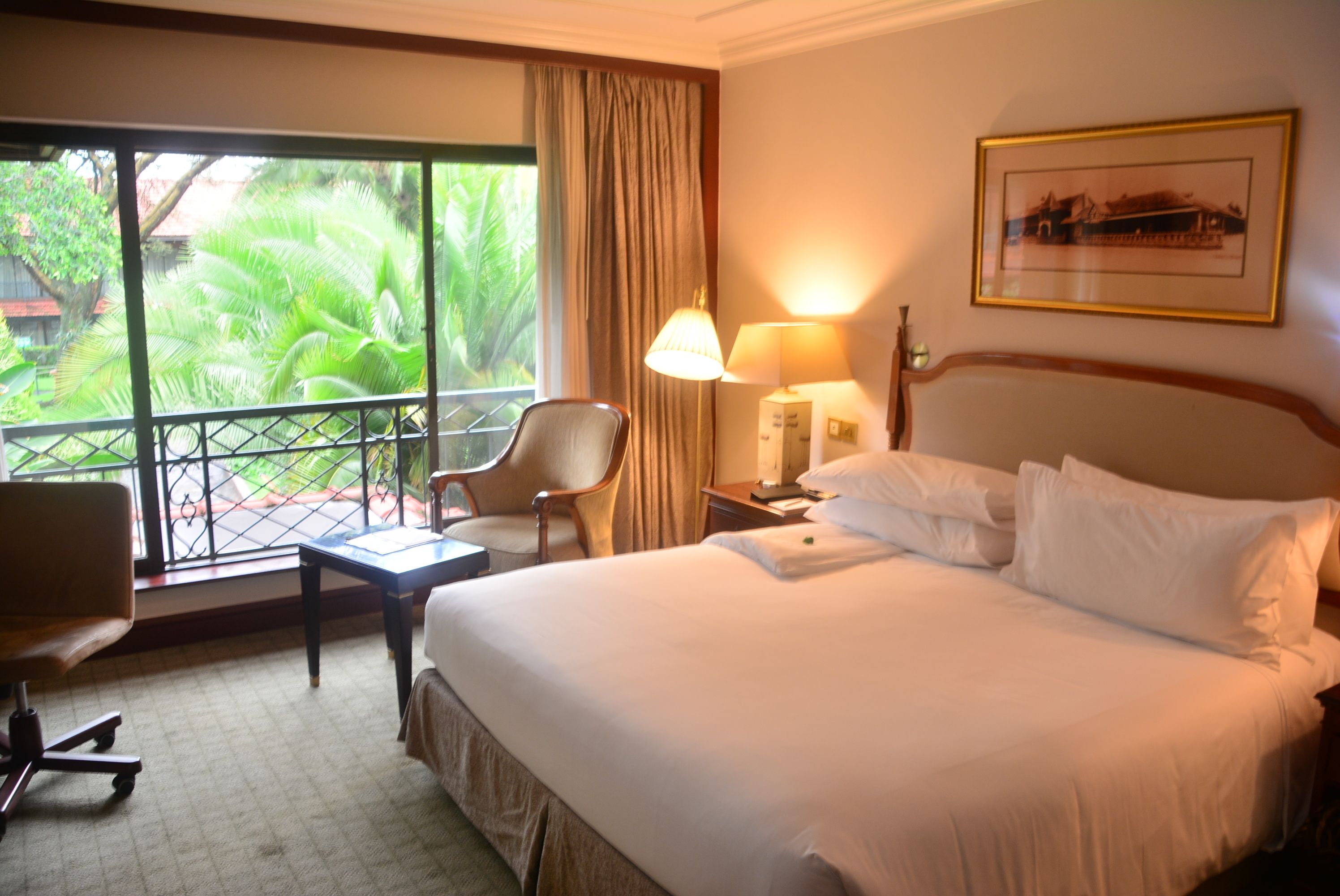 Habitación de hotel con una cama grande, un escritorio, una silla, una ventana con vistas a zonas verdes y un cuadro en la pared.
