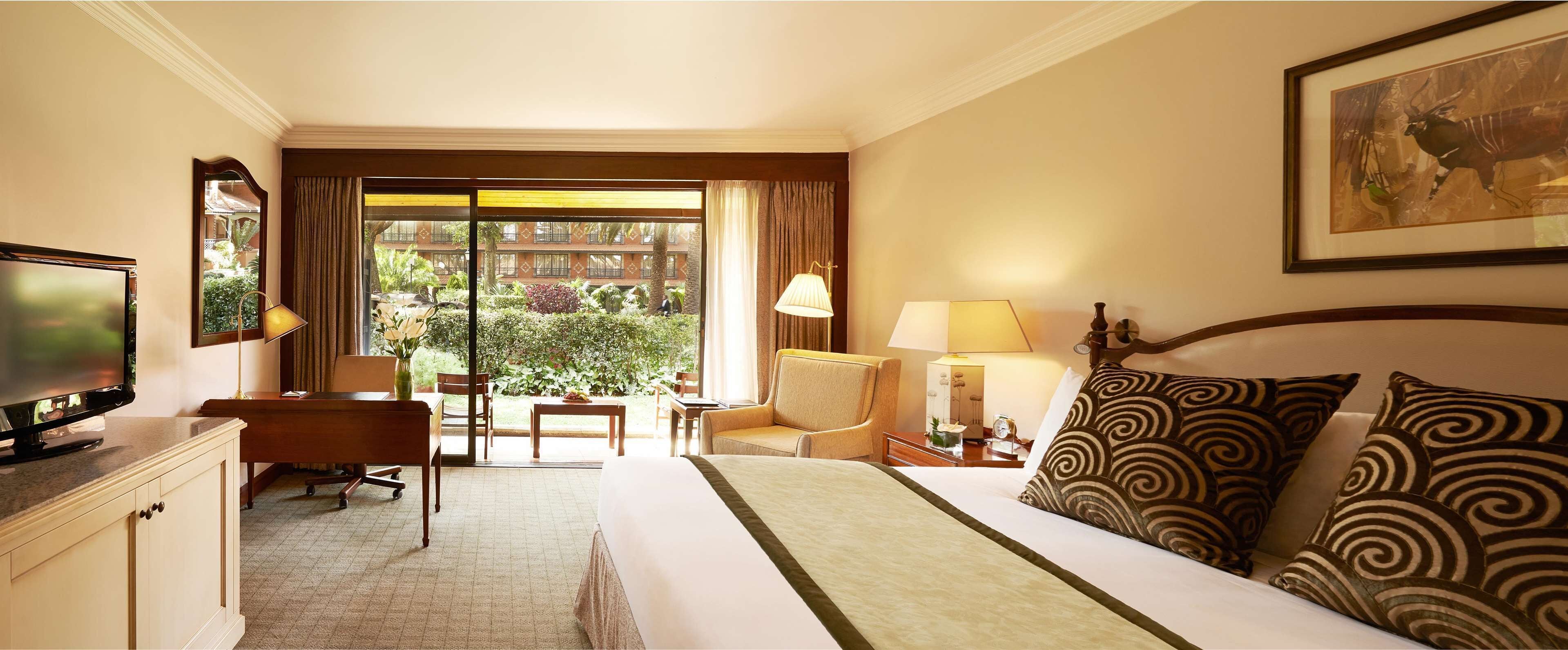 Un cuarto de hotel con cama, escritorio, televisor y vista al jardín por la ventana.