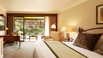 Un cuarto de hotel con cama, escritorio, televisor y vista al jardín por la ventana.