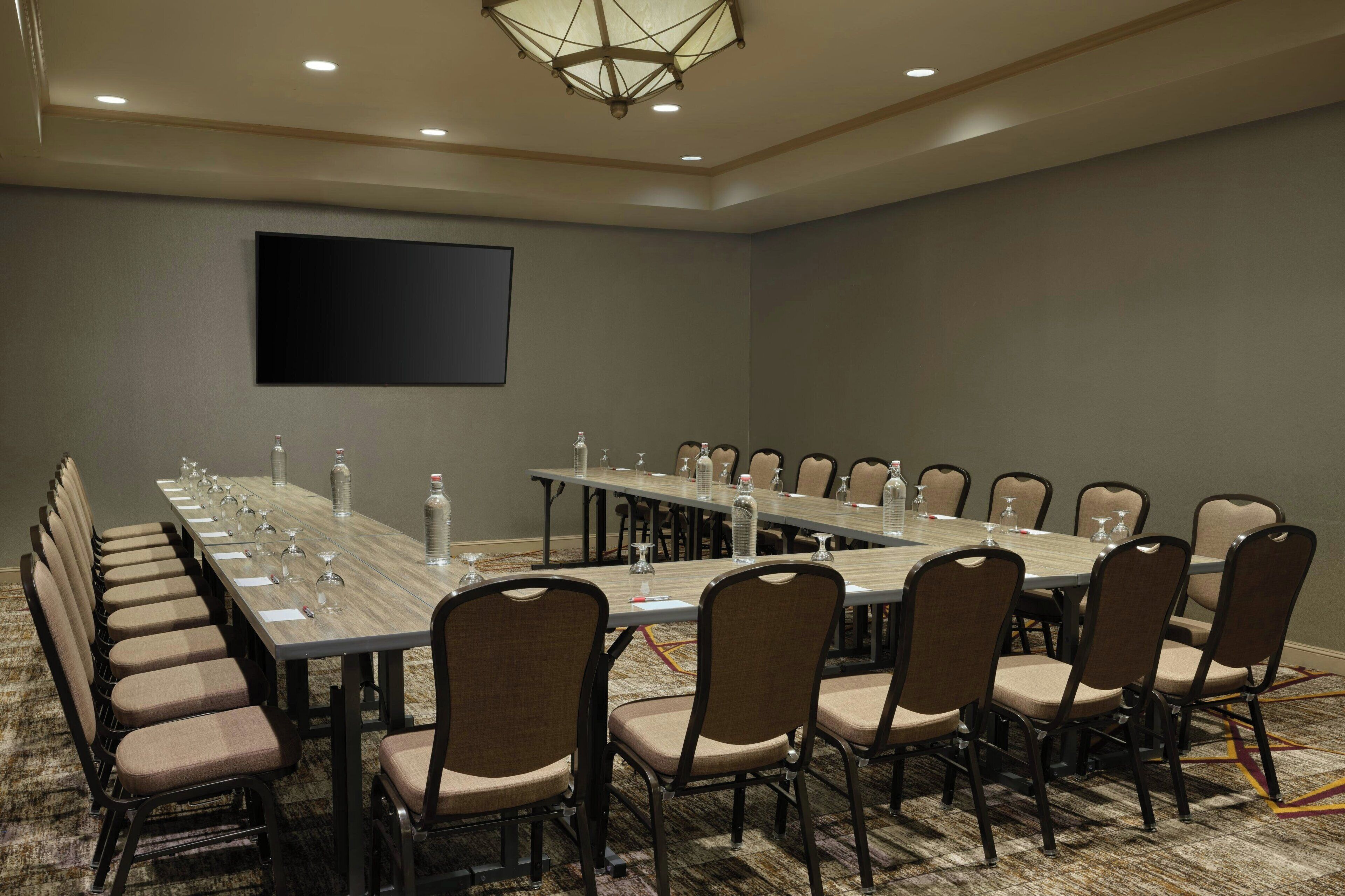 A conference room with a long table, chairs, a flat-screen TV, and a carpeted floor.