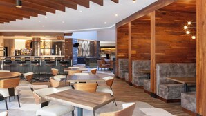 A modern restaurant with wooden accents, multiple seating areas, and a bar in the background.