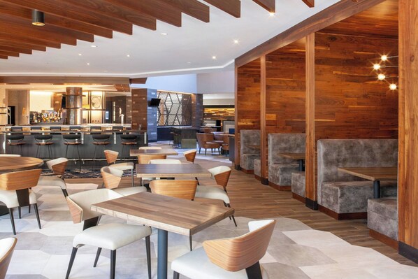 A modern restaurant with wooden accents, multiple seating areas, and a bar in the background. - Marriott Raleigh Durham Research Triangle Park (Durham)