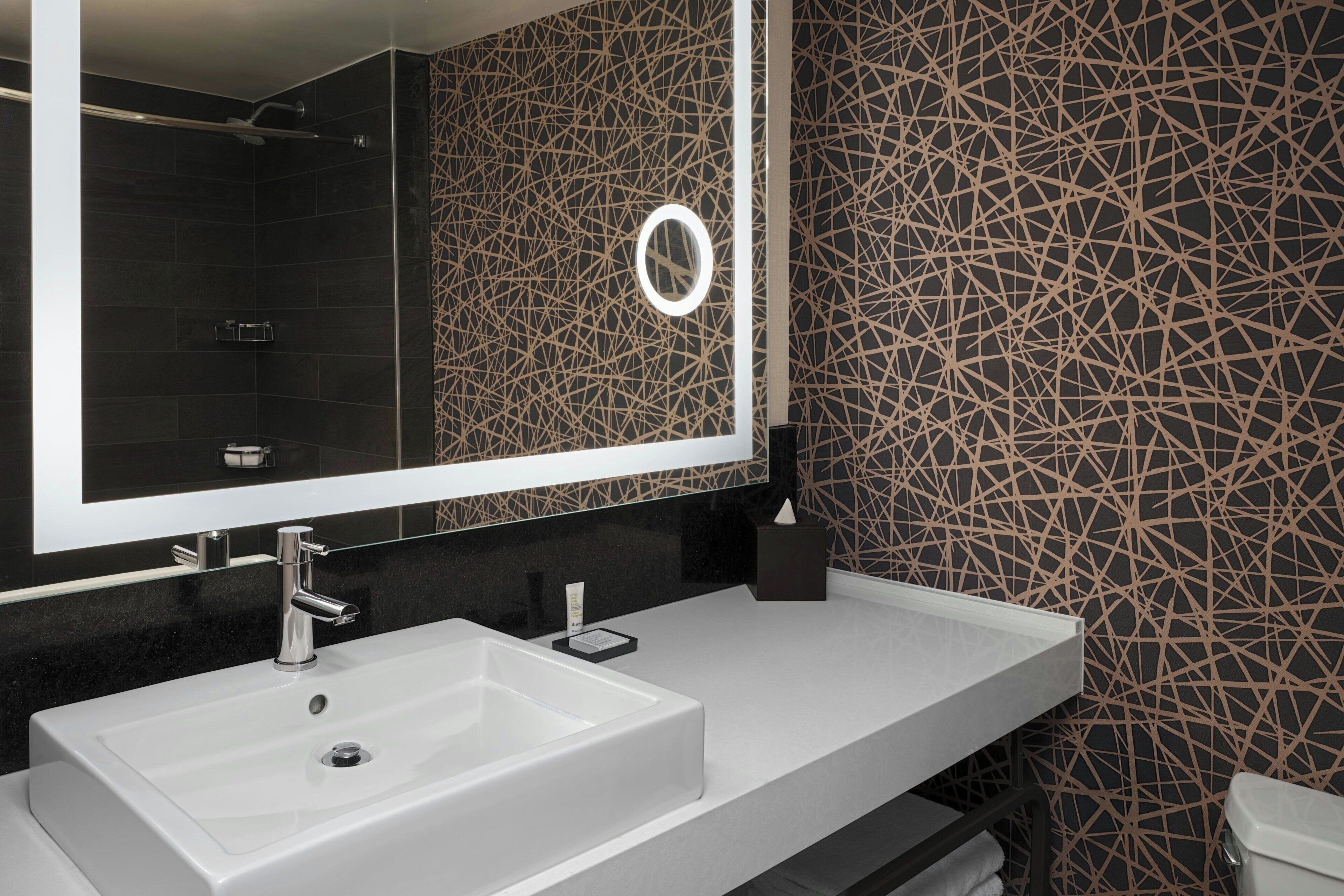 A modern bathroom with a large mirror, a white sink, and a patterned wall.