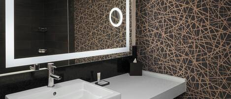 A modern bathroom with a large mirror, a white sink, and a patterned wall.