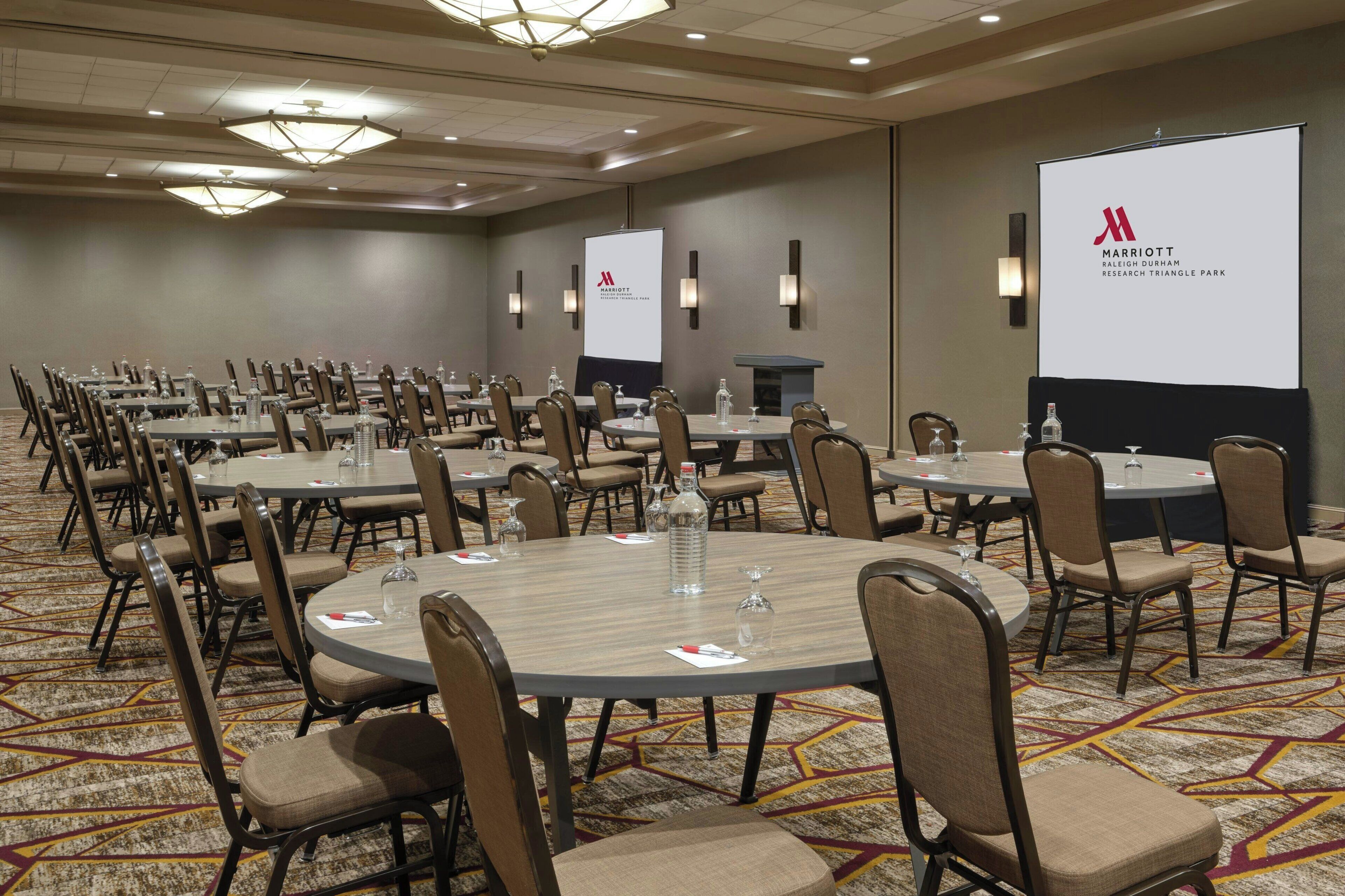 A conference room with multiple round tables, chairs, and a projector screen displaying the Marriott logo.