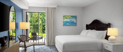 A hotel room with a bed, bedside table, lamp, chair, and a view of greenery through the window.