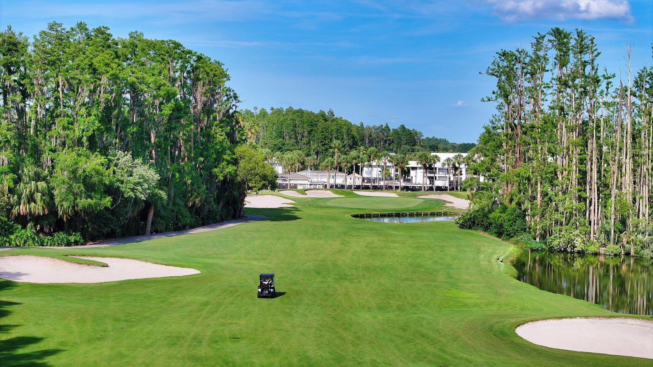 A golf course with a clubhouse, water hazards, and dense trees.