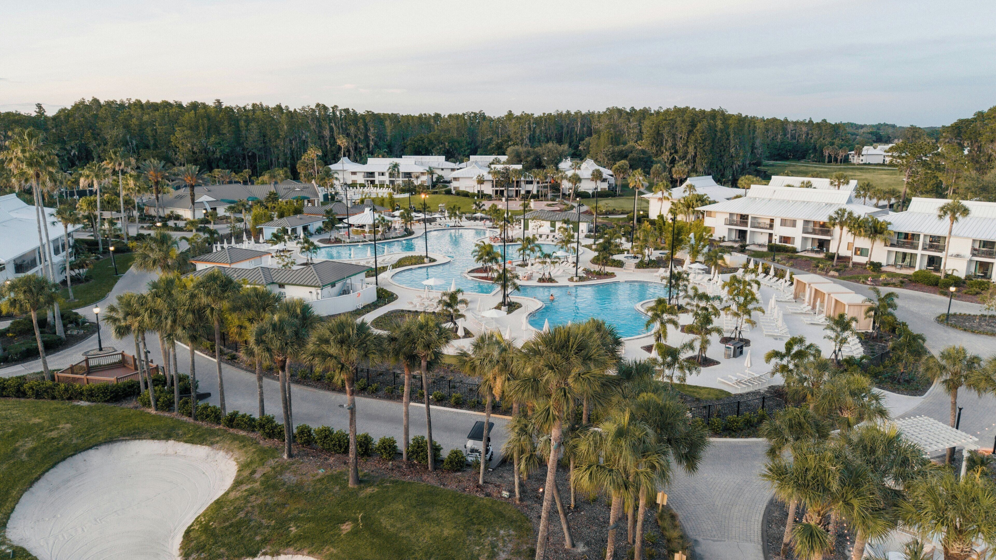 Ein Resort mit einem zentralen Schwimmbad, mehreren Gebäuden und Palmen.