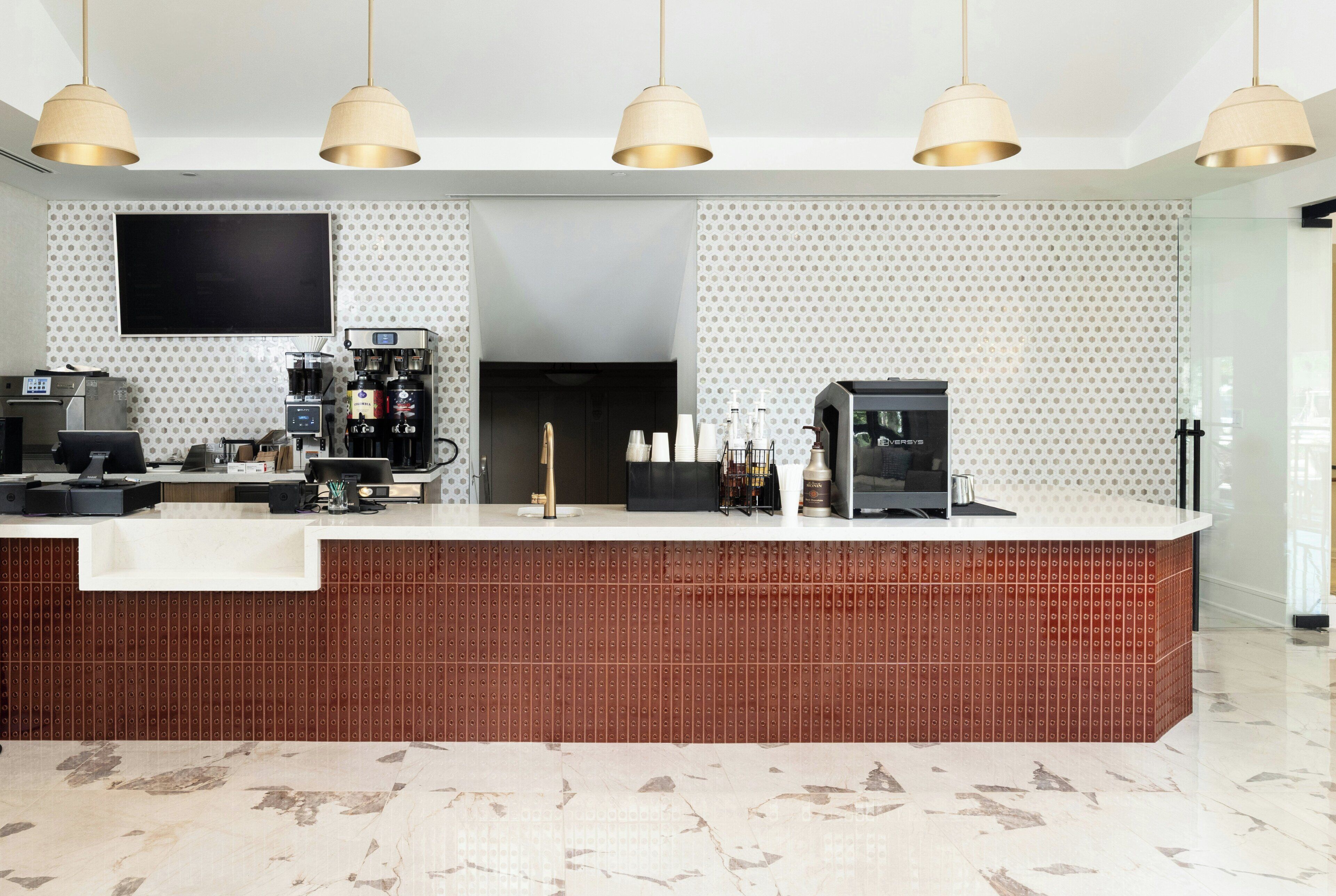 Un área de bar moderna con una cafetera, un refrigerador y un televisor de pantalla plana montado en la pared.