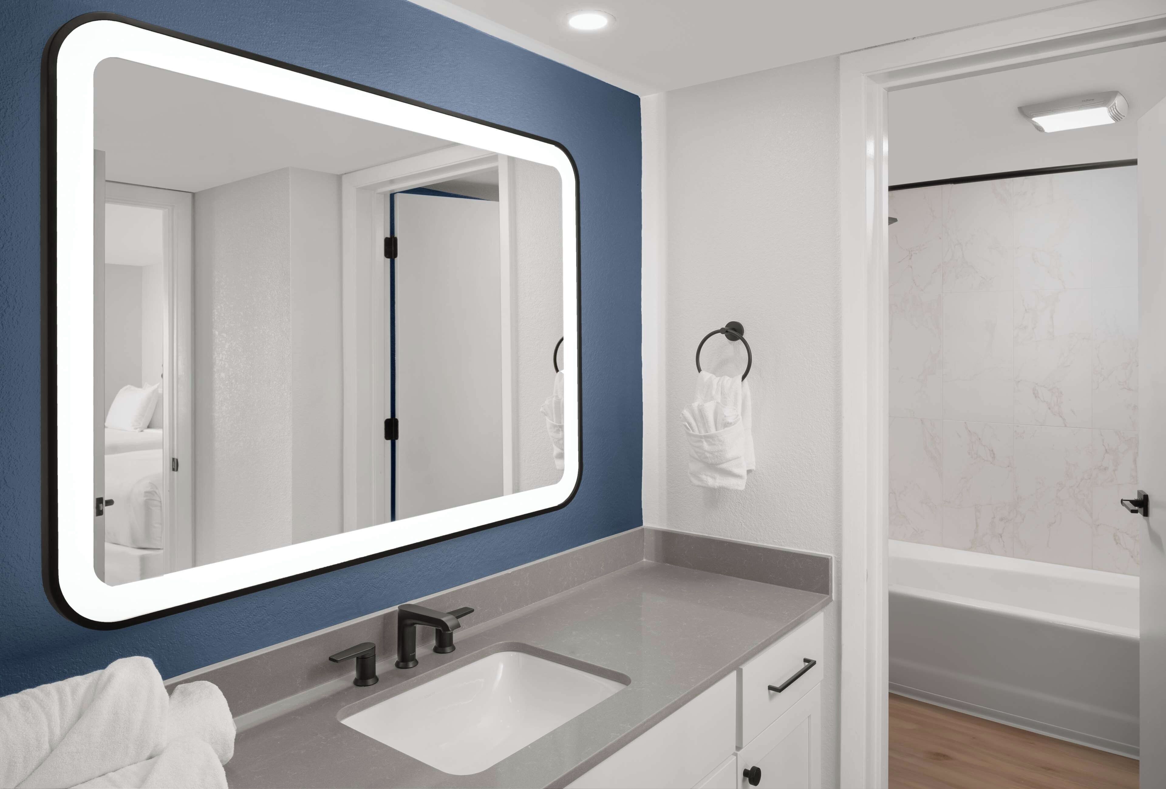 Un baño moderno con un espejo grande, un lavamanos y una zona de ducha.