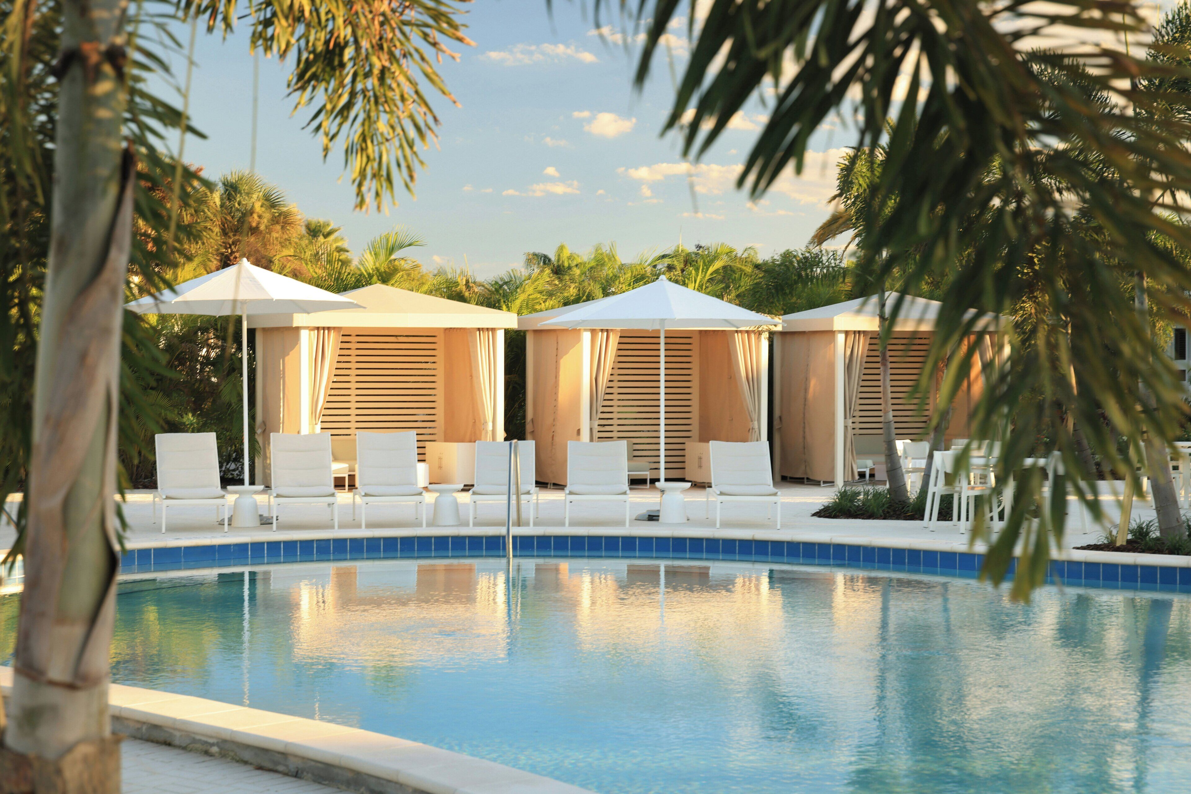 A pool area with lounge chairs and umbrellas, surrounded by palm trees.