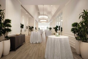 A hotel corridor with round tables covered in white tablecloths, flanked by potted plants and a wooden cabinet. - Saddlebrook Resort (Wesley Chapel)