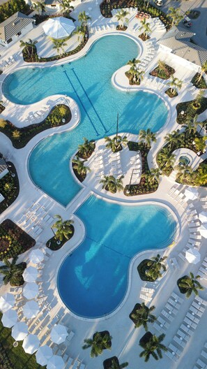 Vista aérea de un complejo turístico con múltiples piscinas interconectadas, zonas de estar con sombrillas y palmeras.