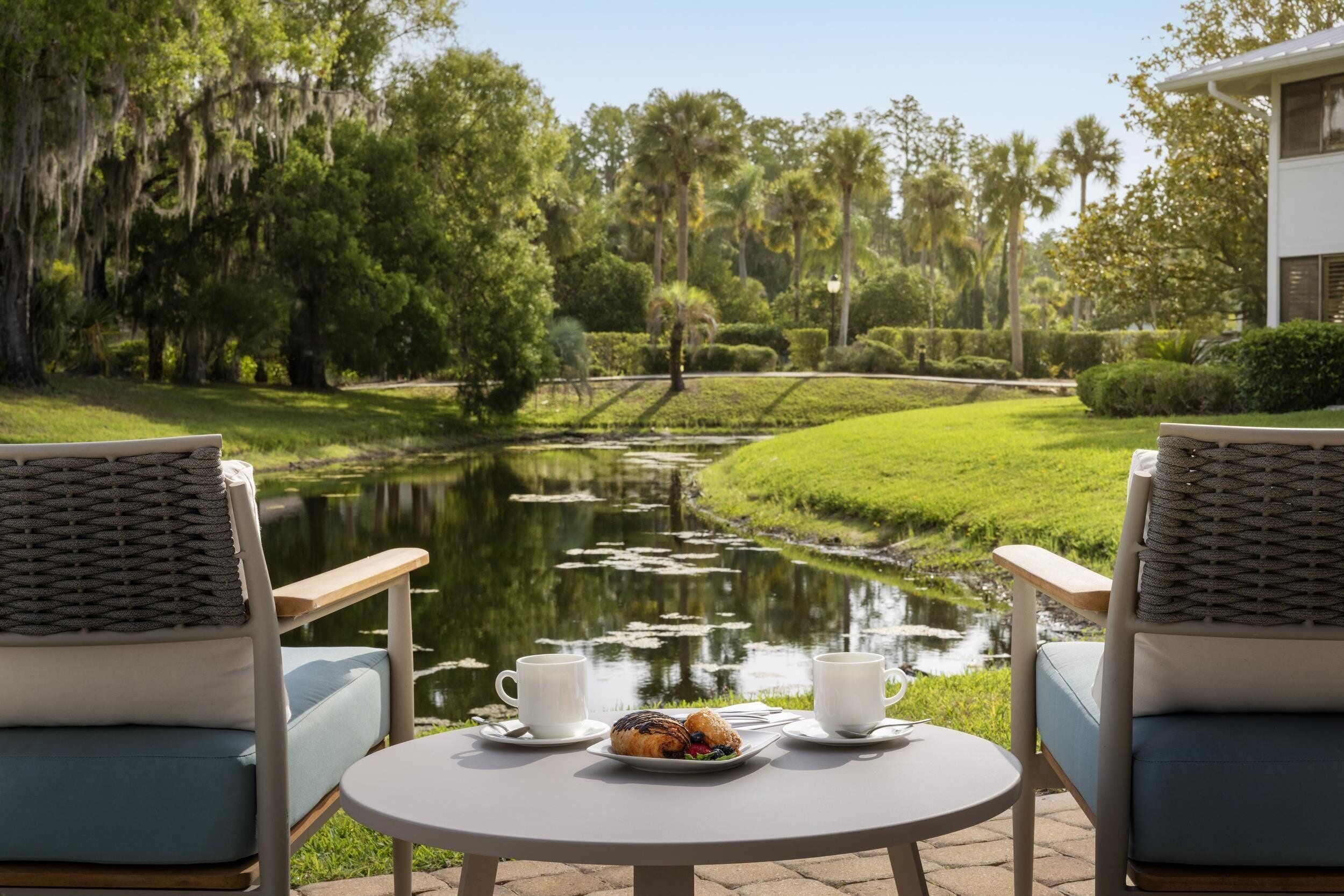 A serene outdoor seating area with two chairs and a table, overlooking a pond and lush greenery.