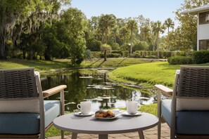 Un tranquilo espacio al aire libre con dos sillas y una mesa, con vistas a un estanque y abundante vegetación.