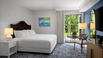Une chambre d’hôtel avec un lit, deux tables de chevet, une chaise, un téléviseur et une vue sur la verdure par la fenêtre.