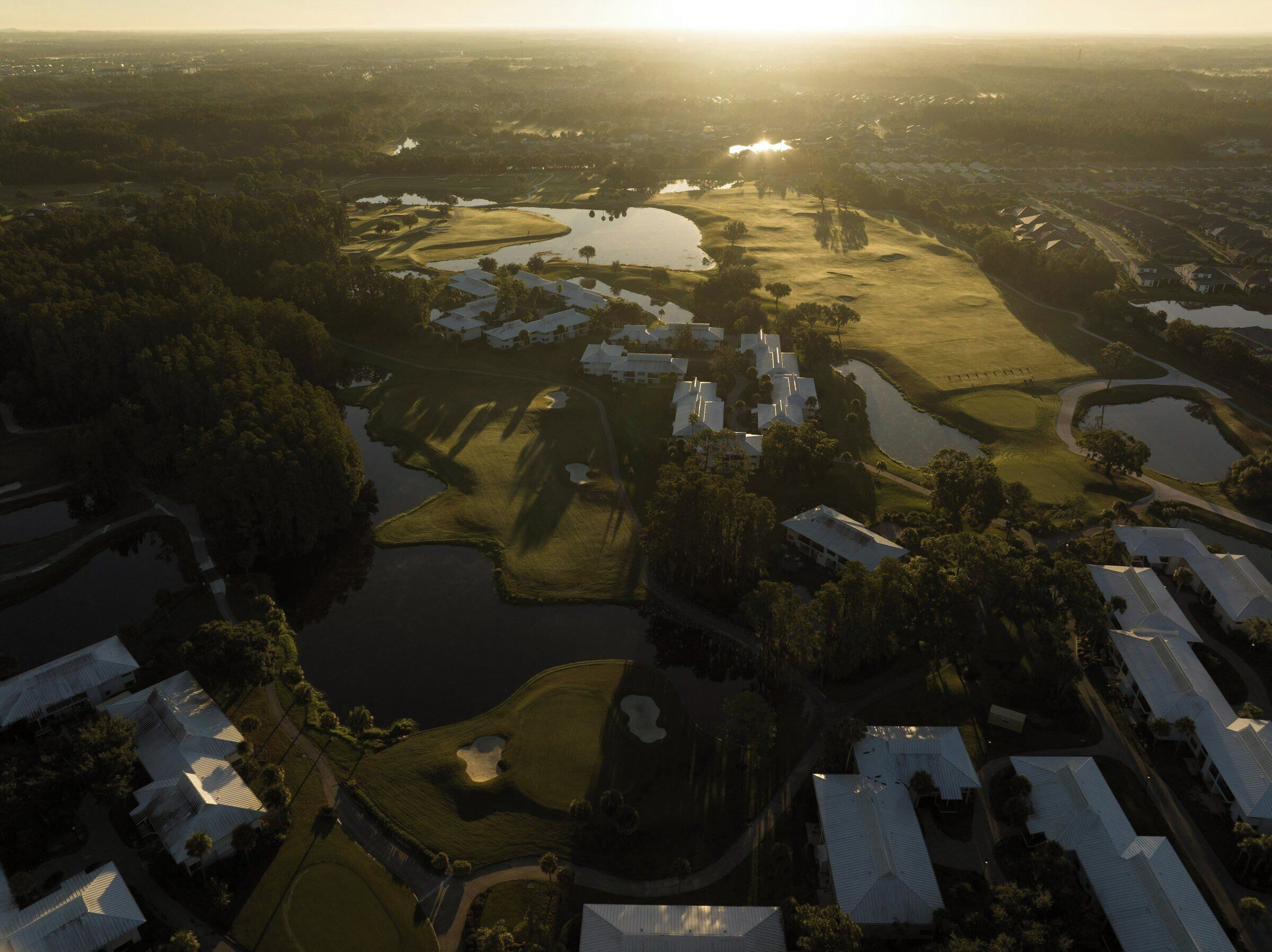 Une vue aérienne d’un terrain de golf comportant de nombreux obstacles d’eau, entouré de bâtiments résidentiels à toits plats.