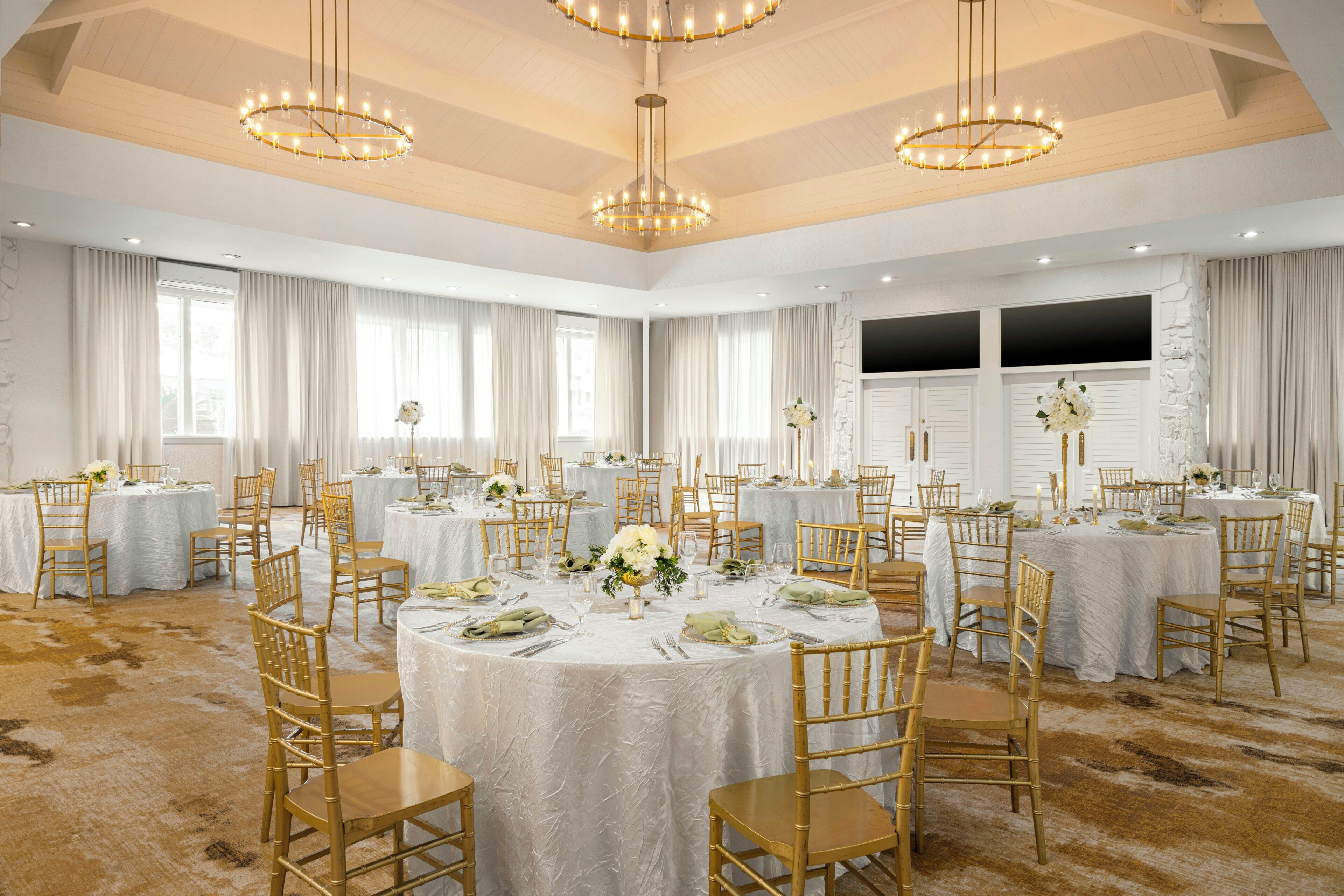 A banquet hall with round tables, chairs, and chandeliers.