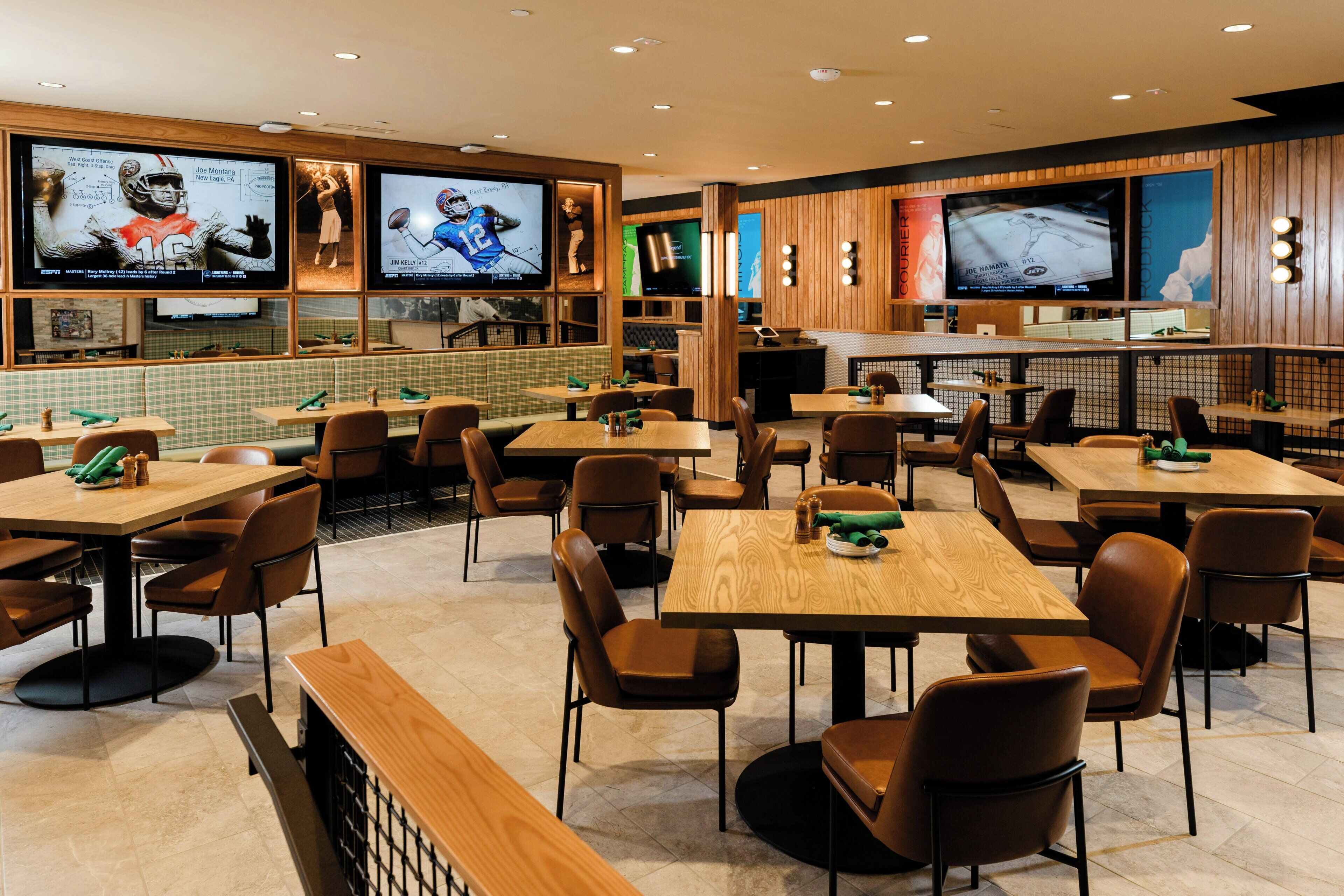A restaurant with multiple tables and booths, sports-themed decor, and televisions displaying sports content.