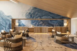 Un vestíbulo moderno con un amplio mural abstracto, zona de estar con sillones de ratán y un mostrador de recepción.