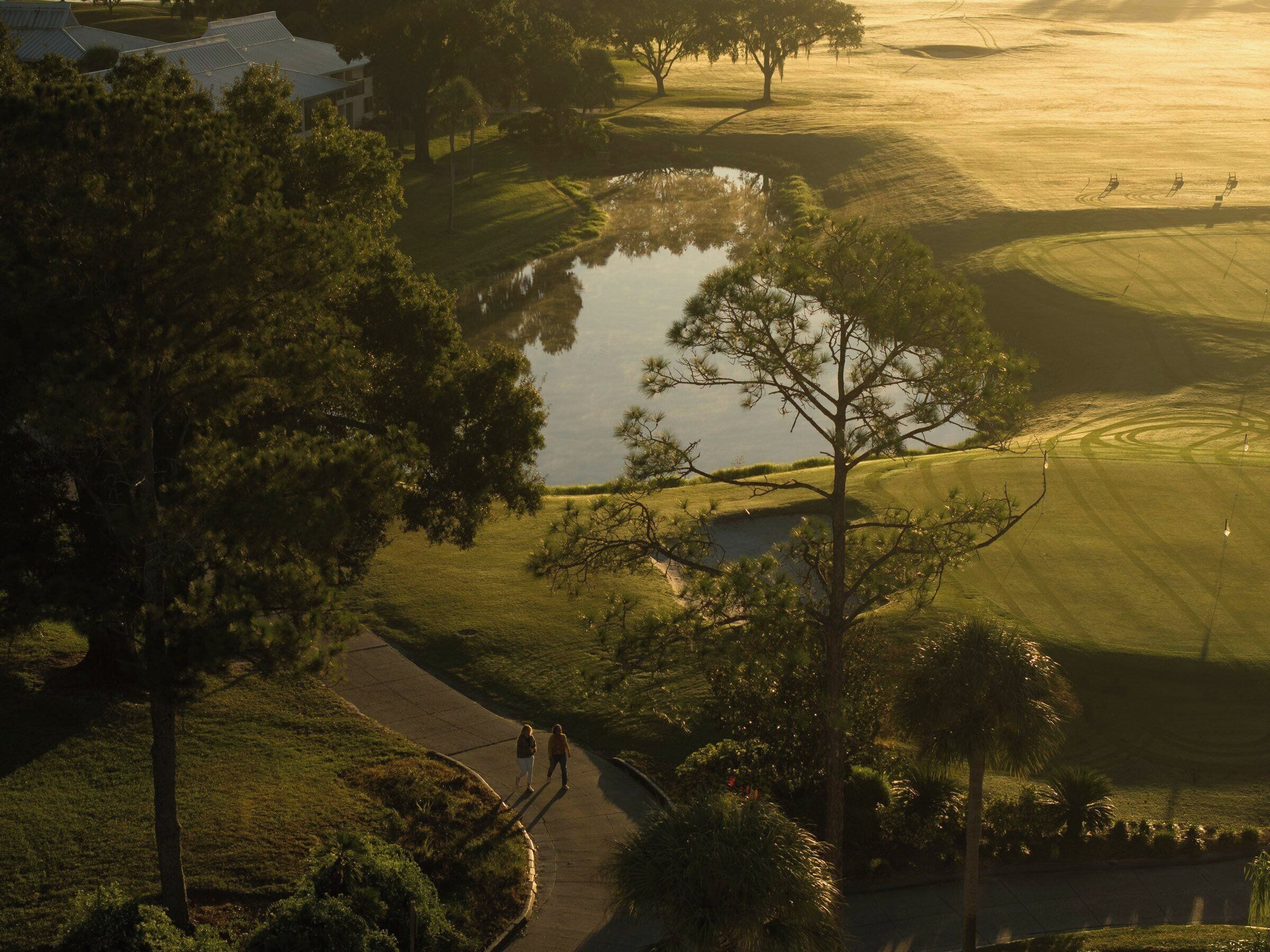 A golf course with a pond, trees, and a walking path.