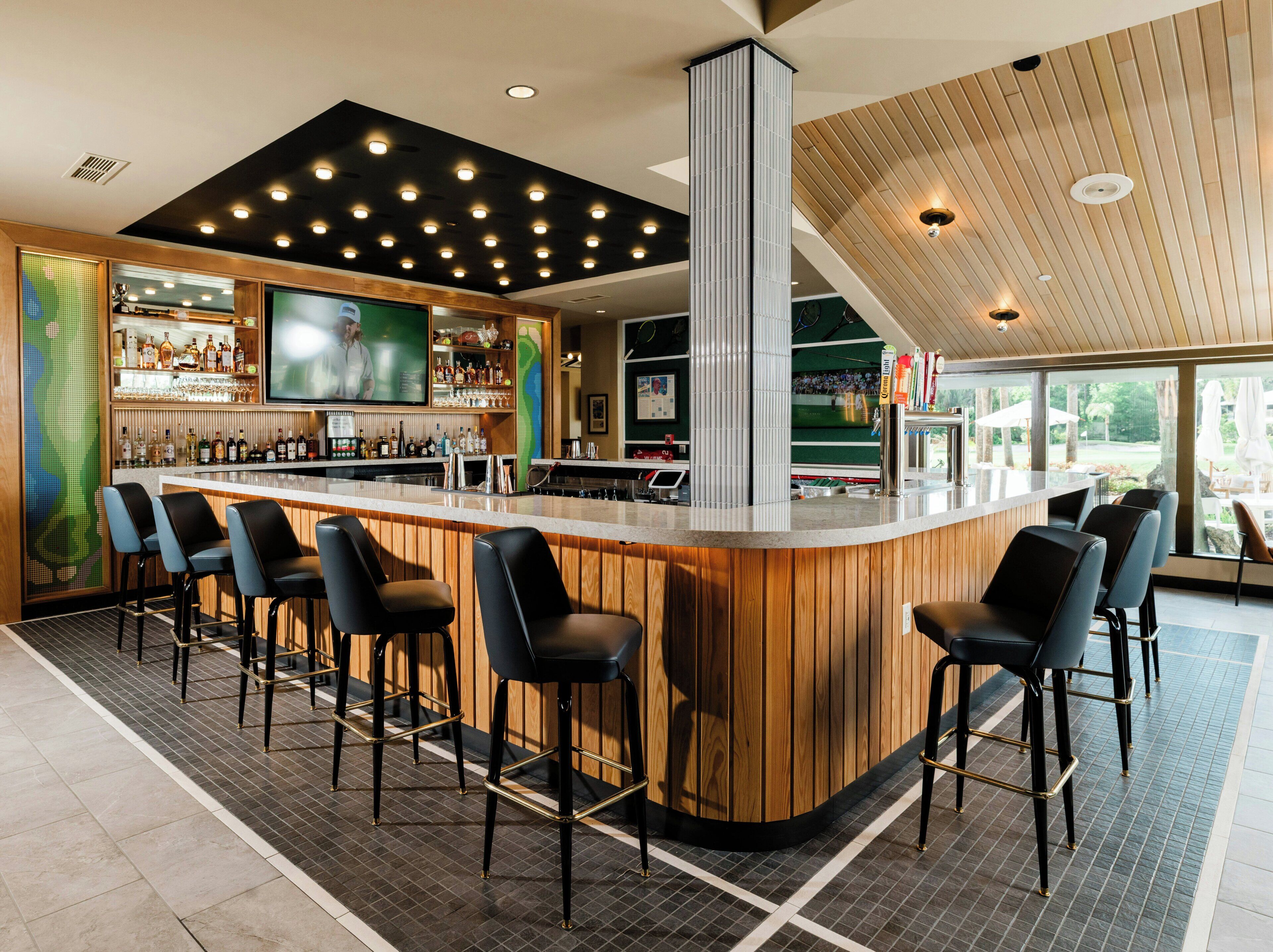 A bar area with a wooden bar counter, multiple bar stools, and a television screen.