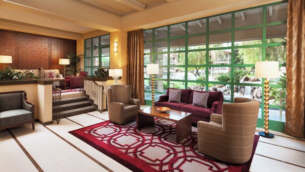 Un hall d’entrée spacieux, doté d’un tapis rouge à motifs, de sièges confortables et de grandes fenêtres offrant une vue sur l’extérieur.