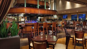 Un restaurant doté d’un bar, de meubles en bois et d’une grande plante en pot.