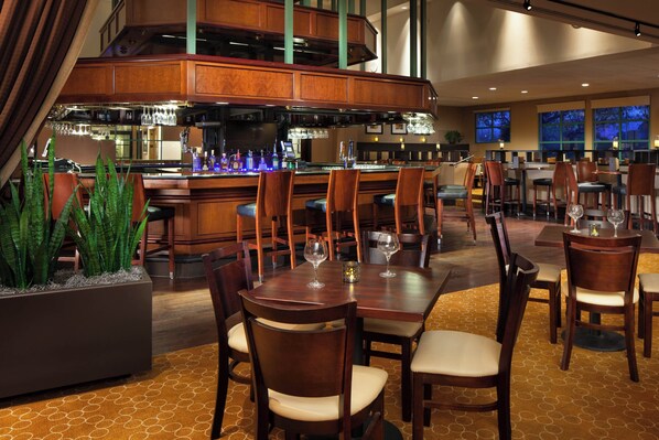A restaurant with a bar area, wooden furniture, and a large potted plant. - Sheraton San Jose Silicon Valley (Milpitas)