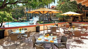 Un espace extérieur aménagé pour les repas, avec des tables et des chaises, une piscine et des parasols.
