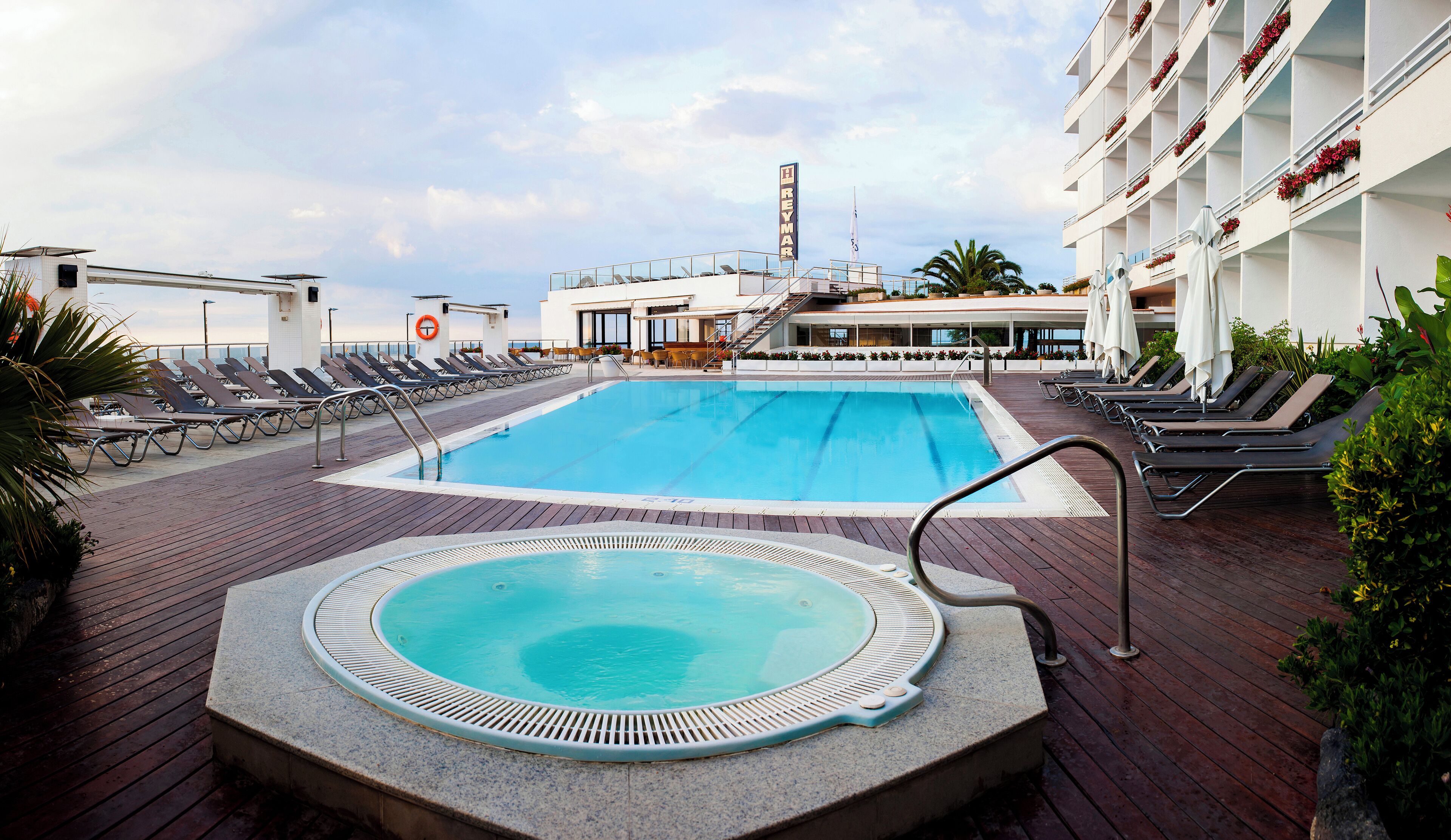Uma área de piscina com espreguiçadeiras, hidromassagem e um salva-vidas.