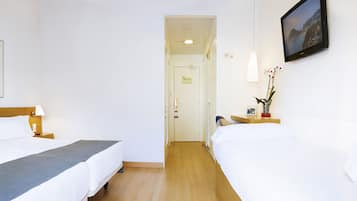 Habitación de hotel con dos camas, un cuadro enmarcado de un velero, una lámpara de noche, una mesita con un florero y un televisor montado en la pared.