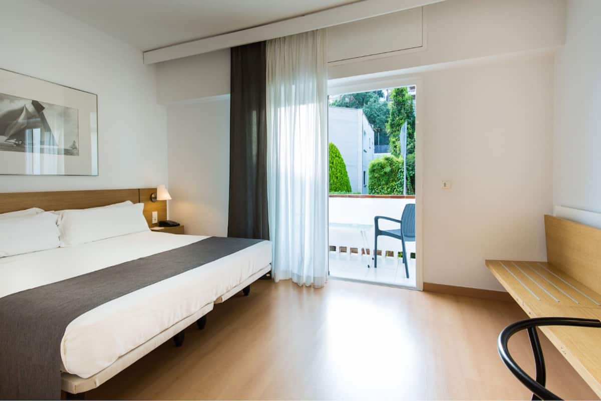 Een hotelkamer met een bed, nachtkastje, lamp en uitzicht op het balkon.