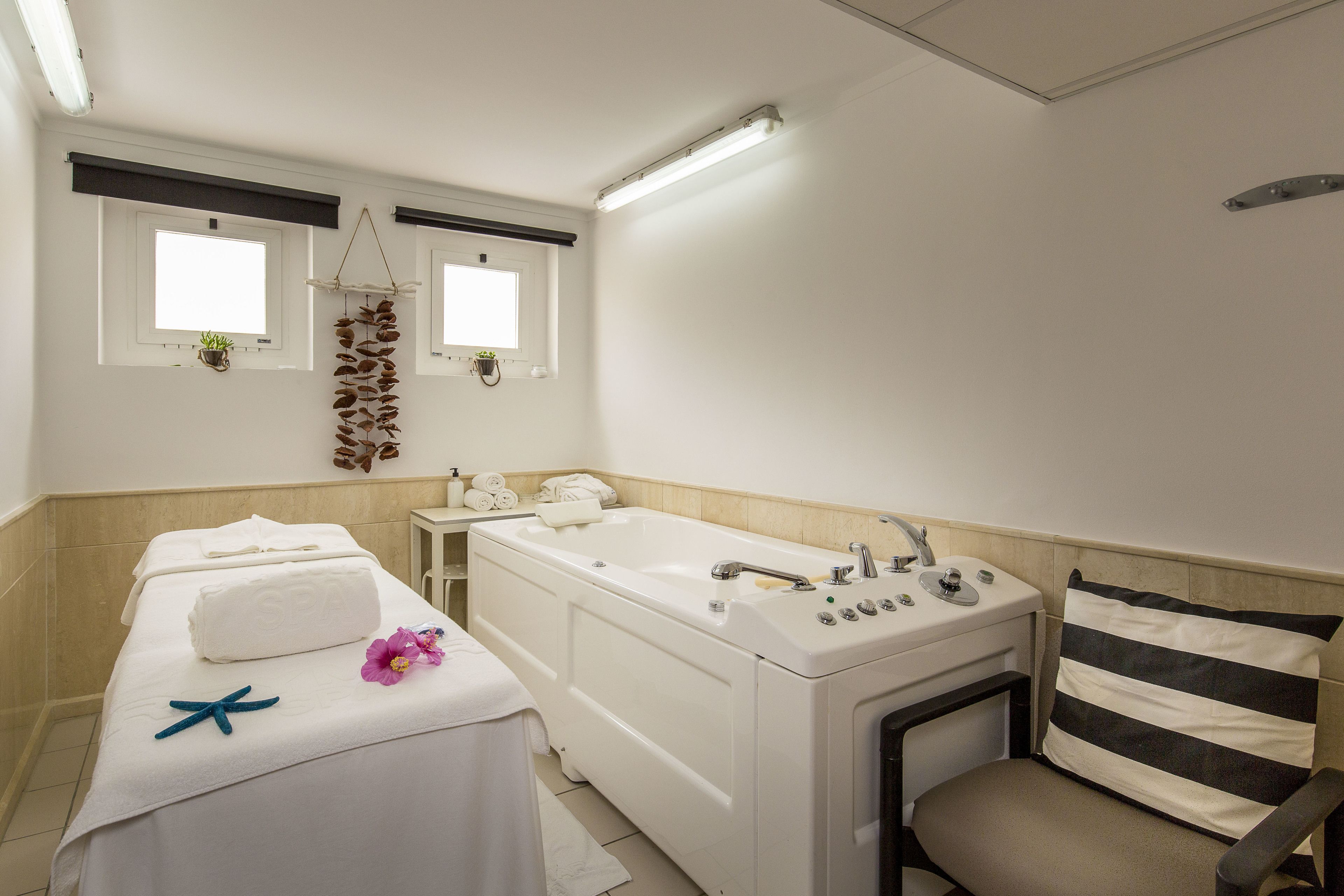 Un bany net i modern amb una banyera, un lavabo i una cadira. Hi ha tovalloles i una estrella de mar al llit.