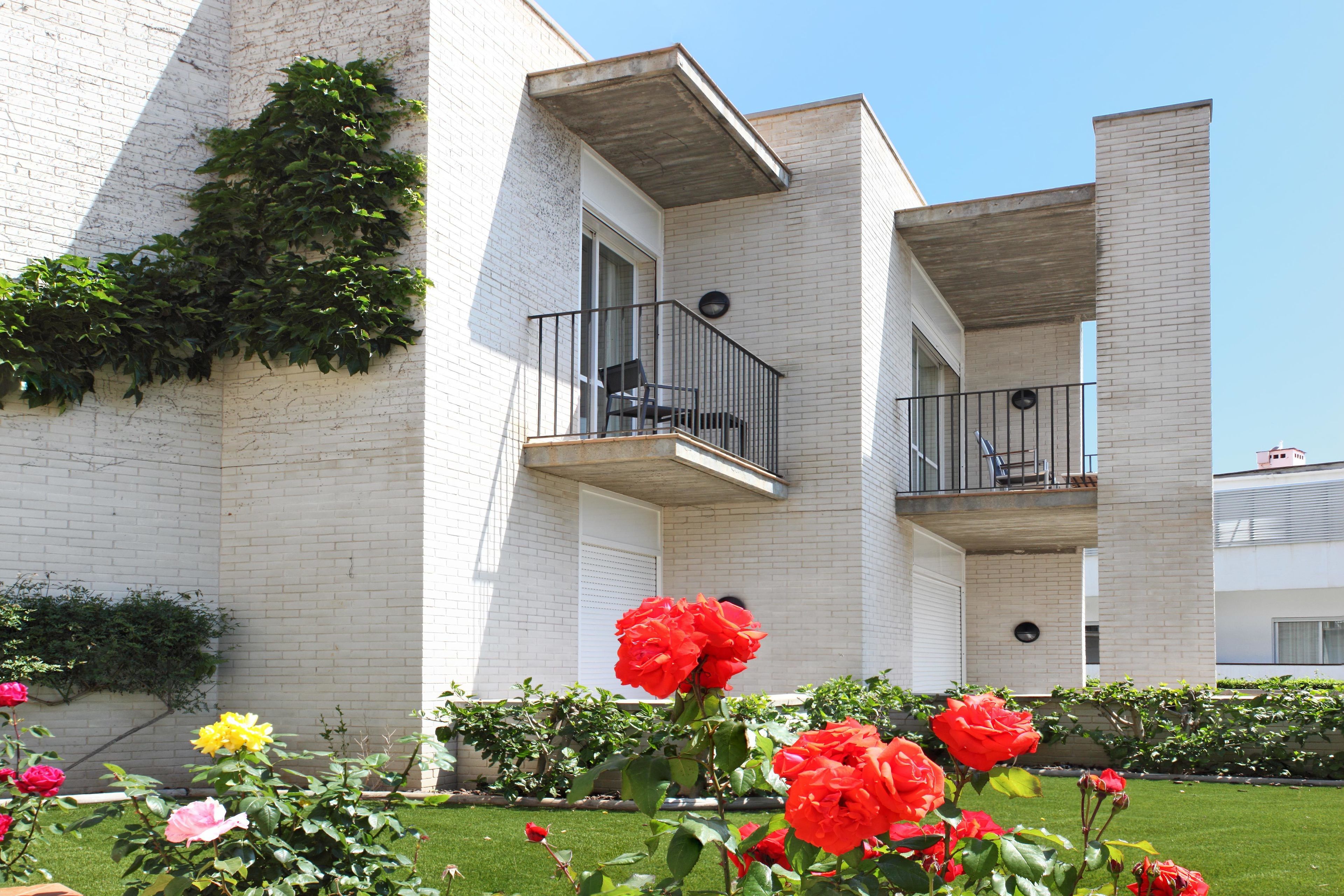 A white brick building with balconies and a garden with flowers.
