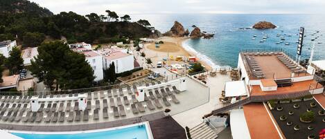 Un hotel frente a la playa con piscina, tumbonas y vistas al mar.