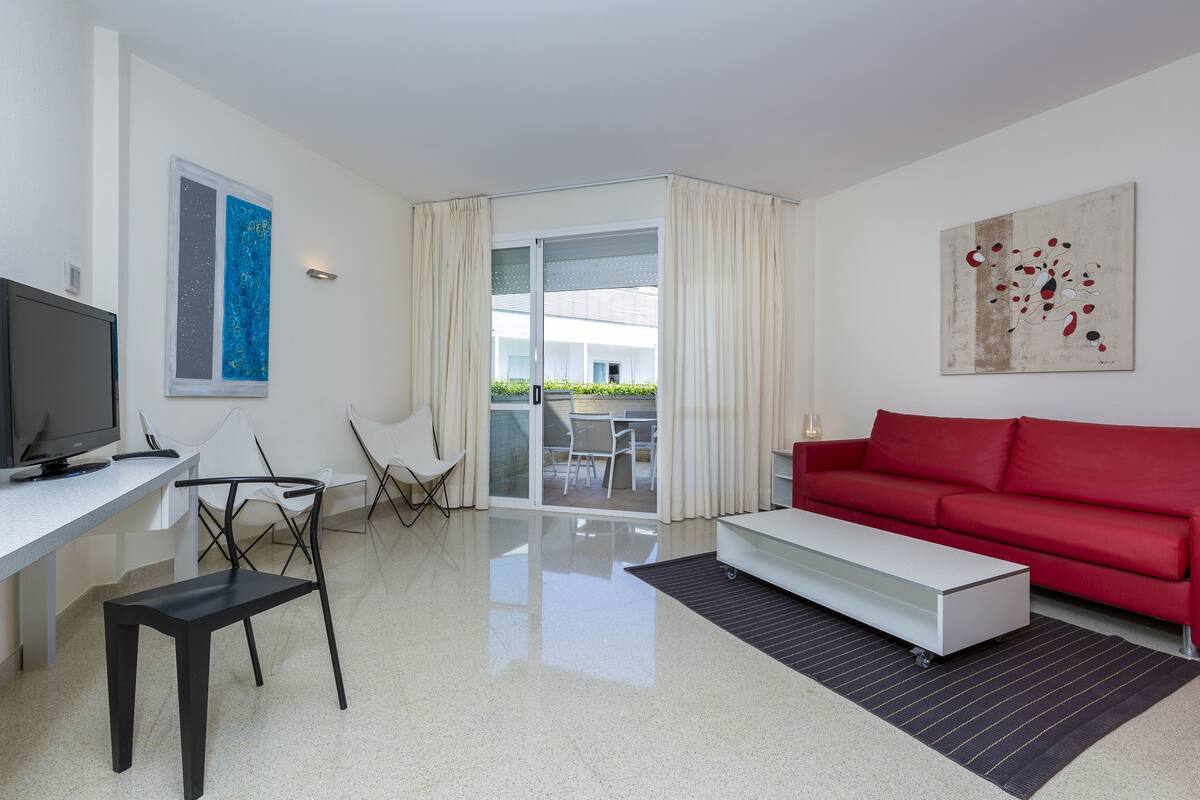 A modern living room with a red sofa, a white coffee table, a TV, and a dining area with chairs and a table.