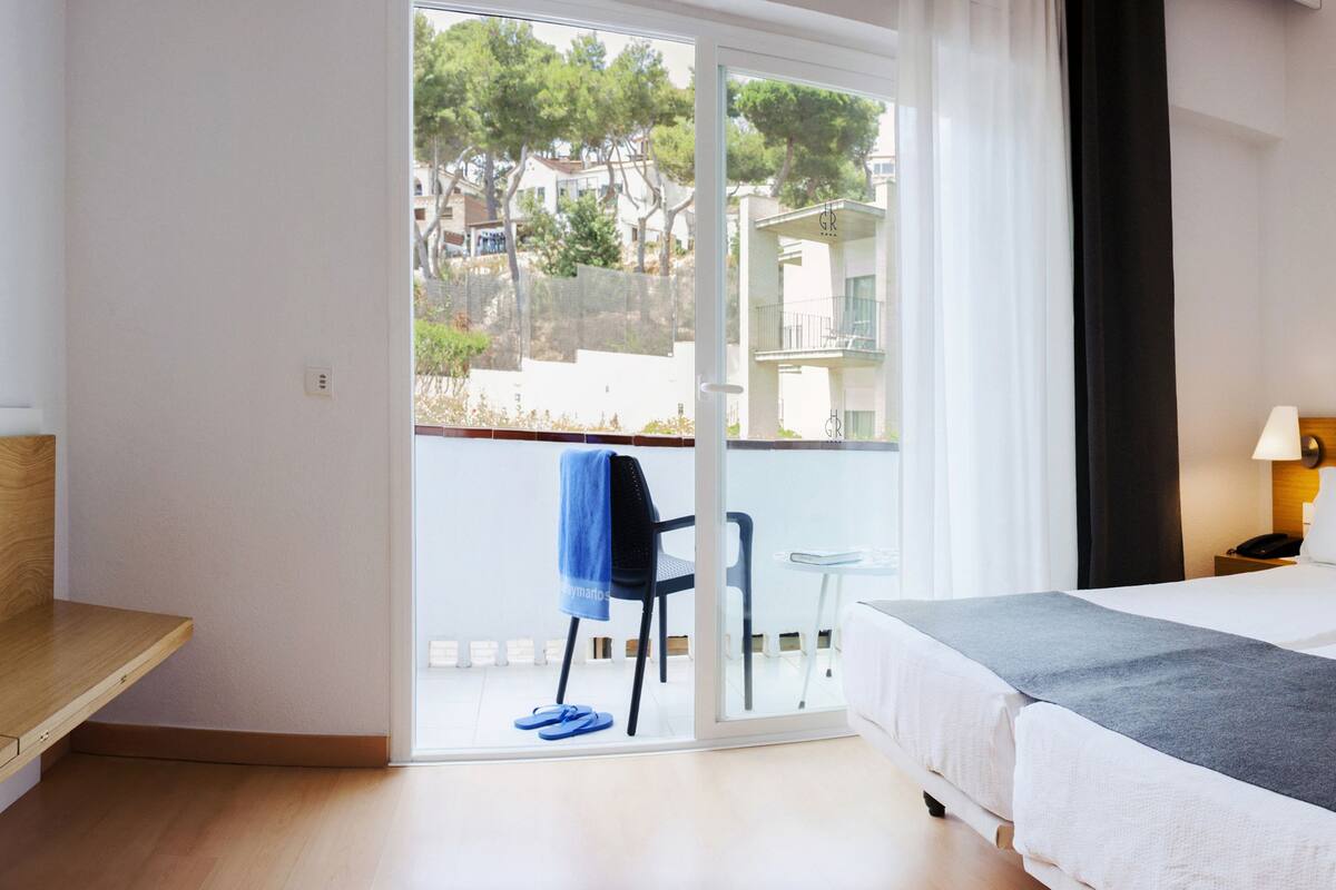 Een hotelkamer met een bed, een stoel, een bureau, een lamp en een schilderij aan de muur.