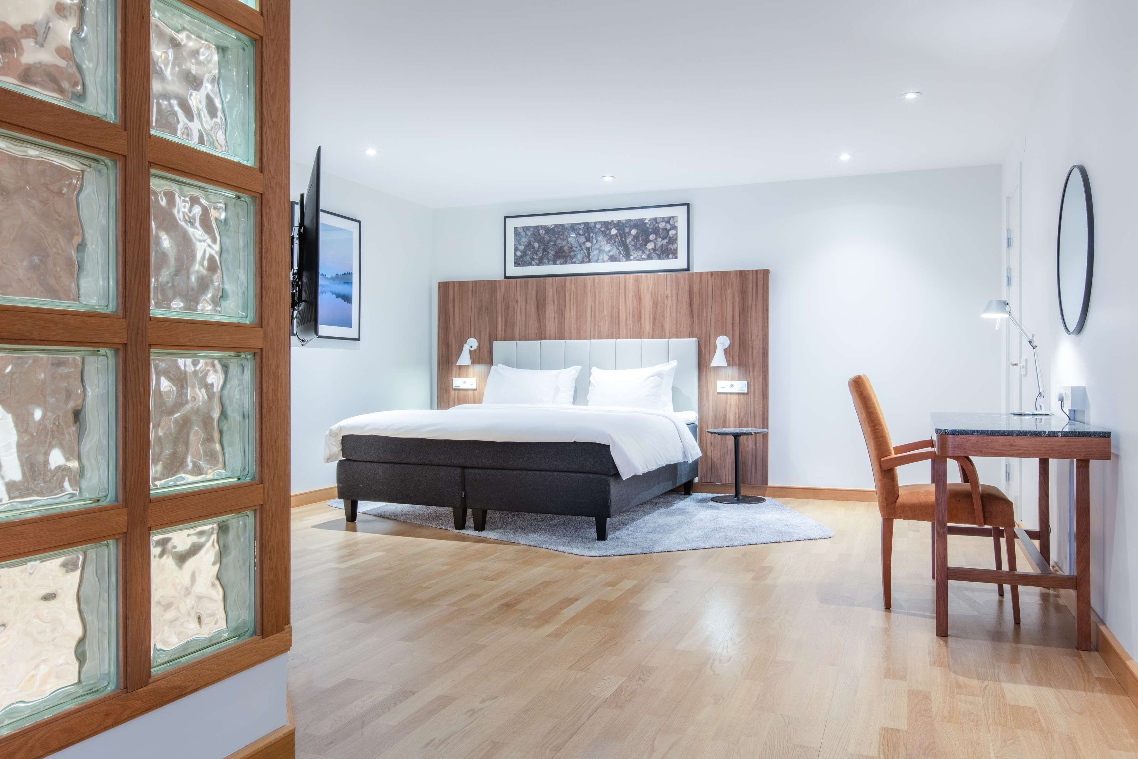A modern bedroom with a bed, bedside tables, a desk, and a chair.