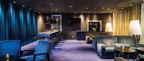 Habitación de hotel con zona de bar, asientos y televisor.