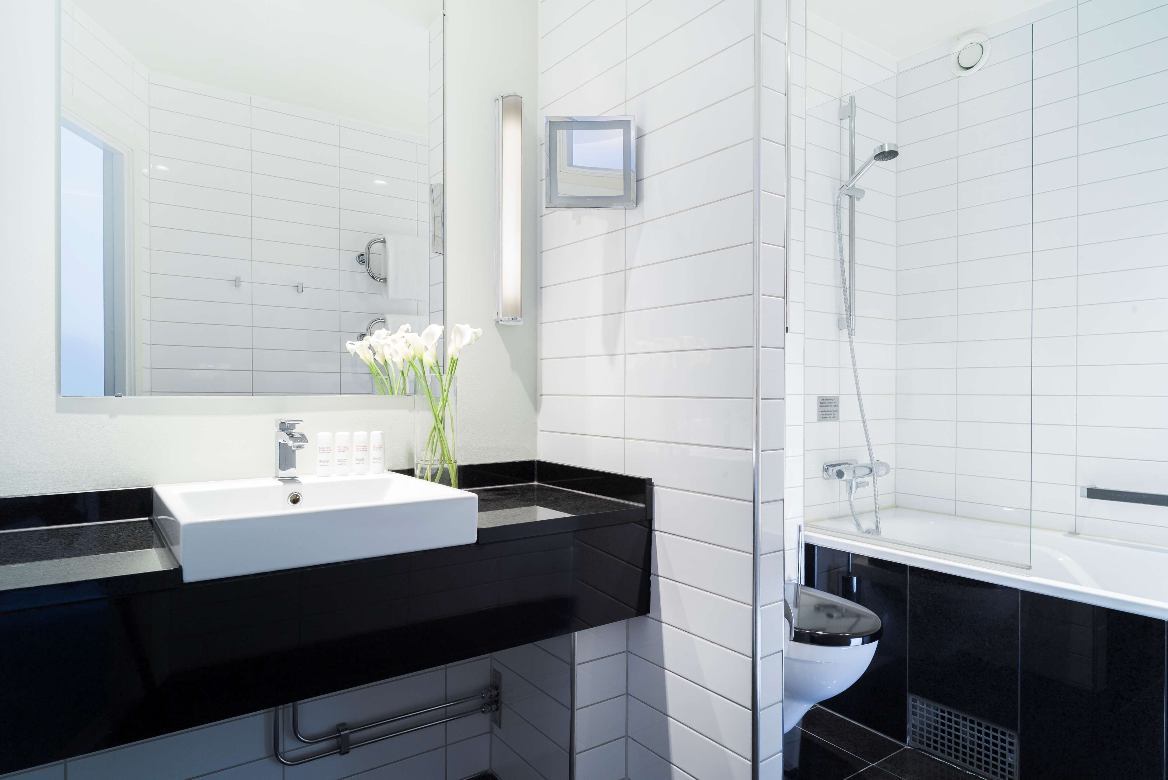 Un baño moderno con un lavamanos blanco, encimera negra y cabina de ducha con mampara de vidrio.