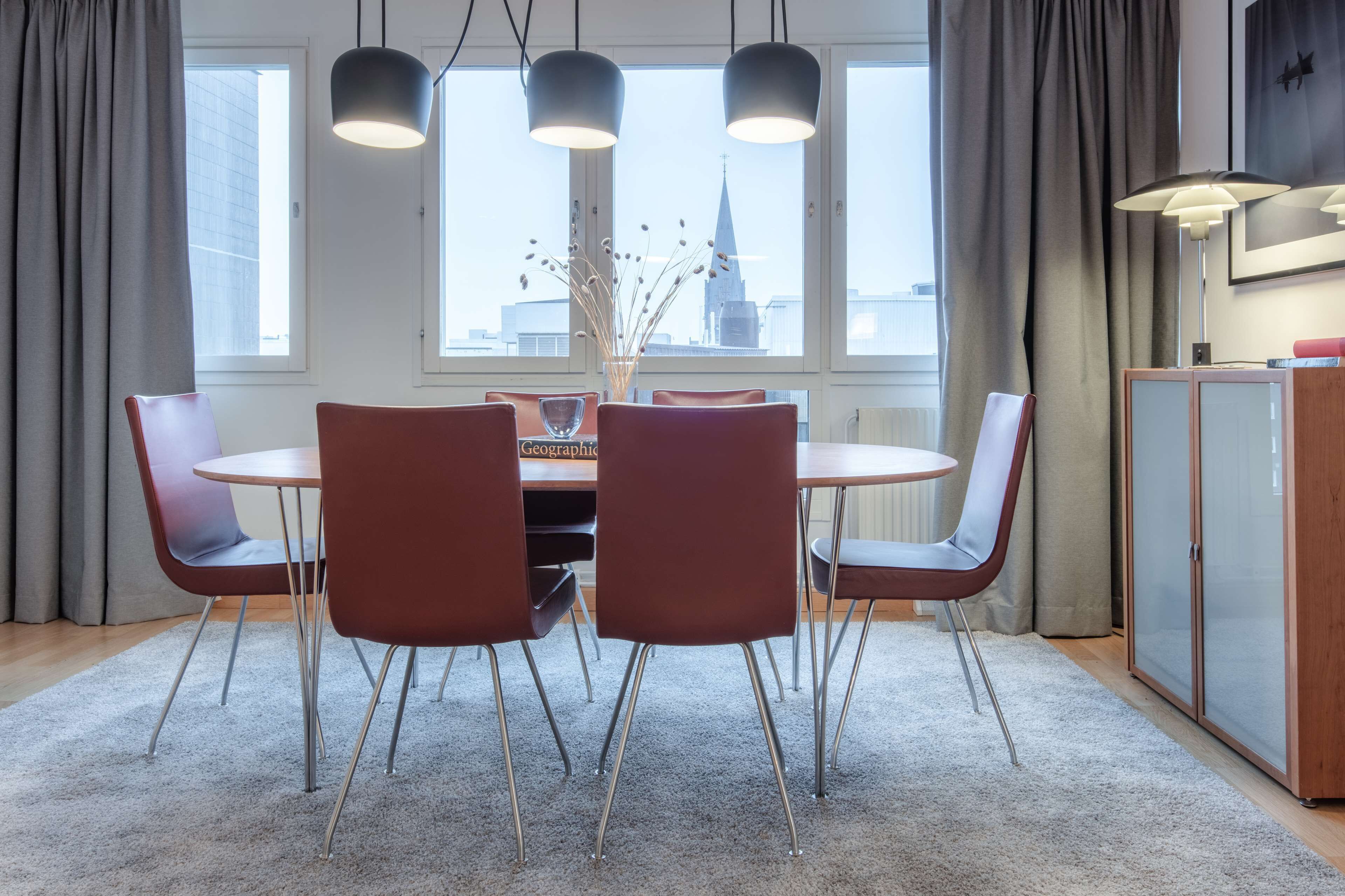 A dining area with a round table, four chairs, and a vase with branches.