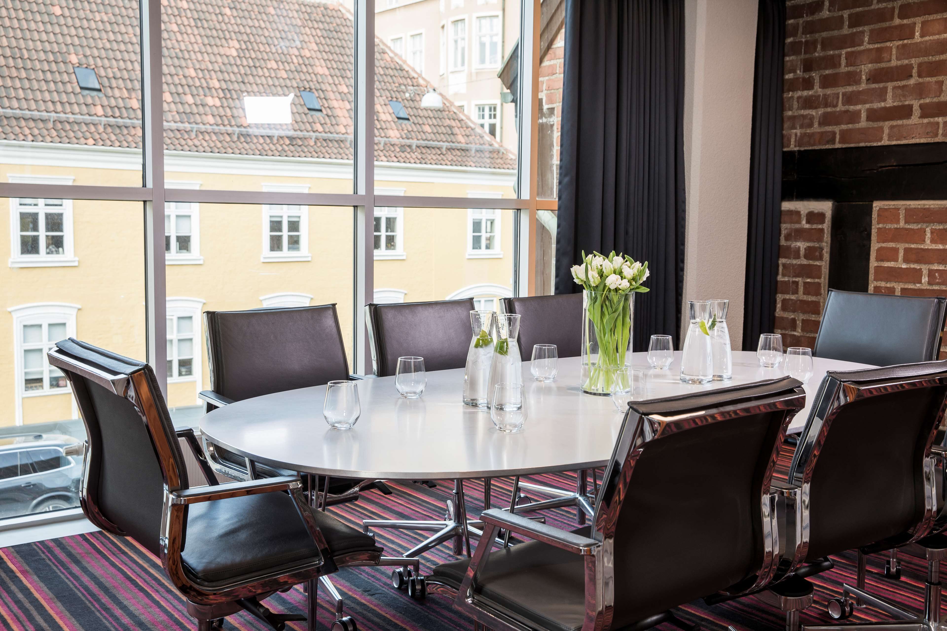 Een vergaderruimte met een ronde tafel, zes stoelen en een uitzicht op gebouwen door grote ramen.