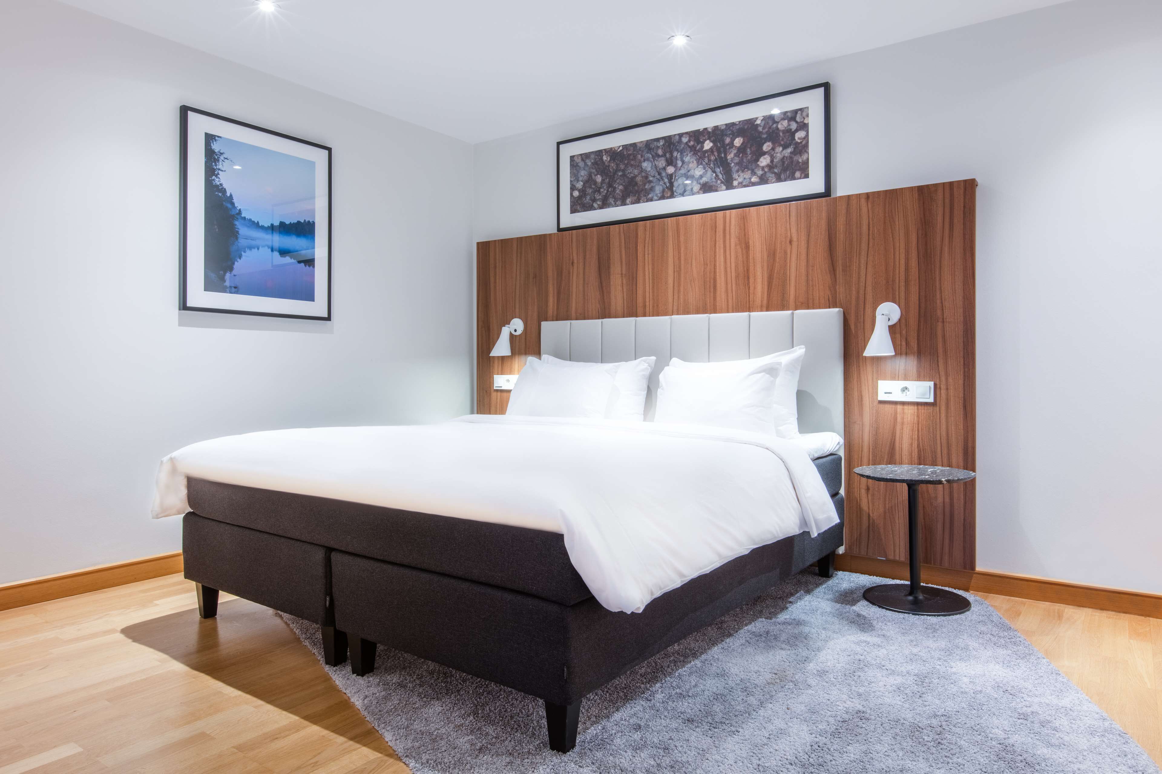 Un dormitorio moderno con una cama grande, dos mesitas de noche, un cabecero de madera y cuadros enmarcados en las paredes.
