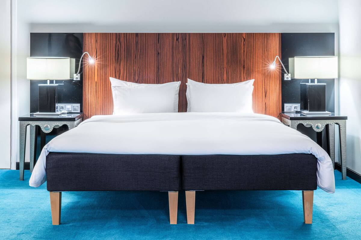 A double bed with a dark headboard and white bedding, two bedside tables with lamps, and a blue carpet.