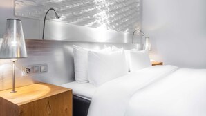 A modern hotel room with a large bed, white bedding, and a unique textured wall above the bed. There are two bedside tables with lamps.