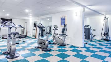 Uma academia com equipamentos de ginástica, piso xadrez e parede com espelhos.