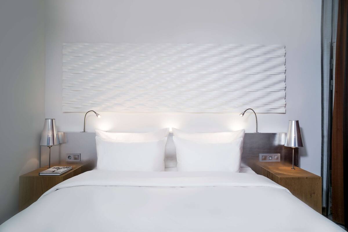 A modern hotel room with a large bed, two bedside tables, and a wall-mounted abstract artwork.